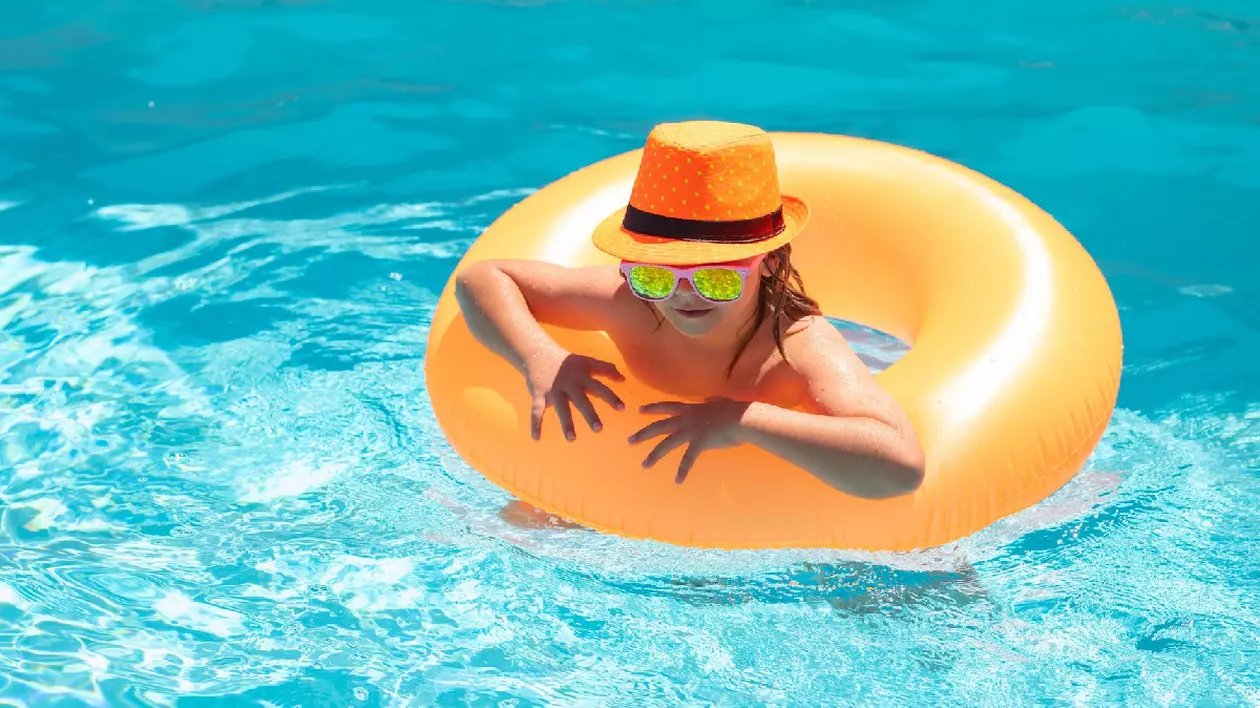 un copil cu un colac mare, galben, se relaxează într-o piscină cu apă albastră, cristalină