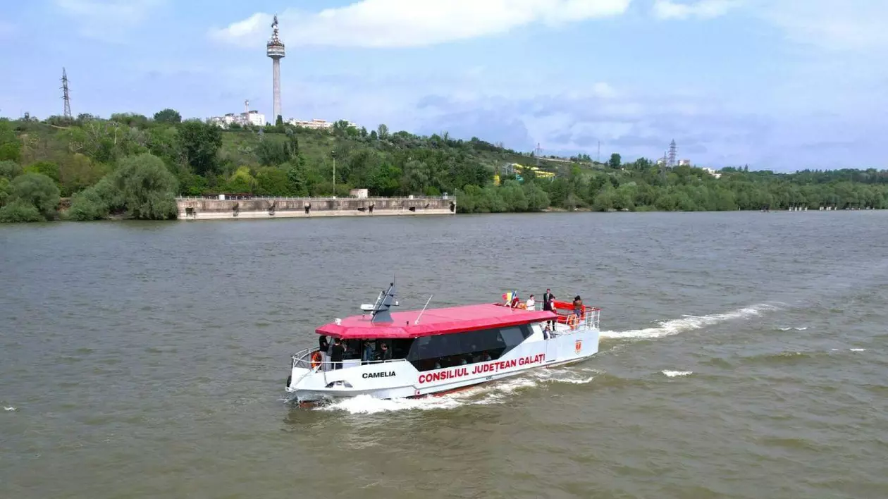 barca cu alb si rosu, apartinand Consilului Județean Galați, in mers pe apă, cu padure in spate,