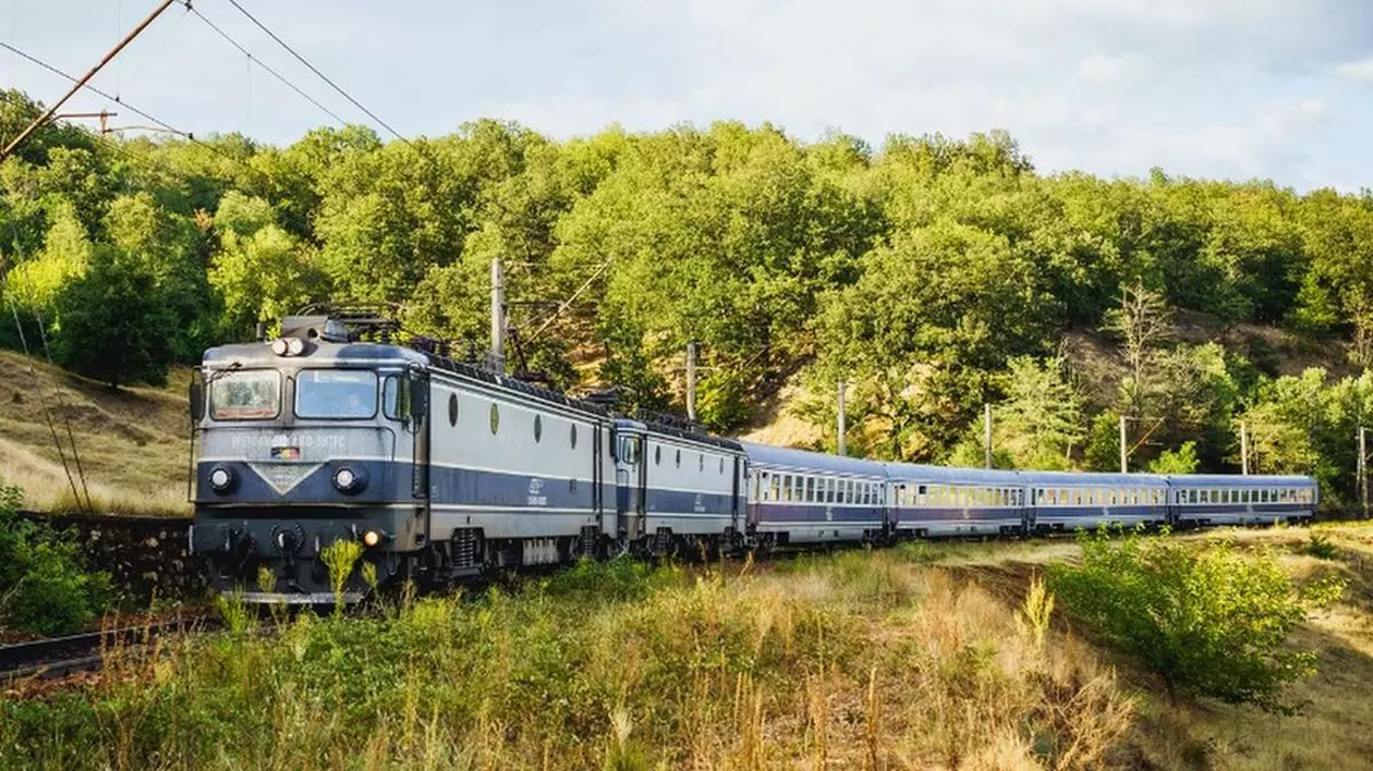 Un tren CFR format din mai multe vagoane merge pe șine într-o zonă verde