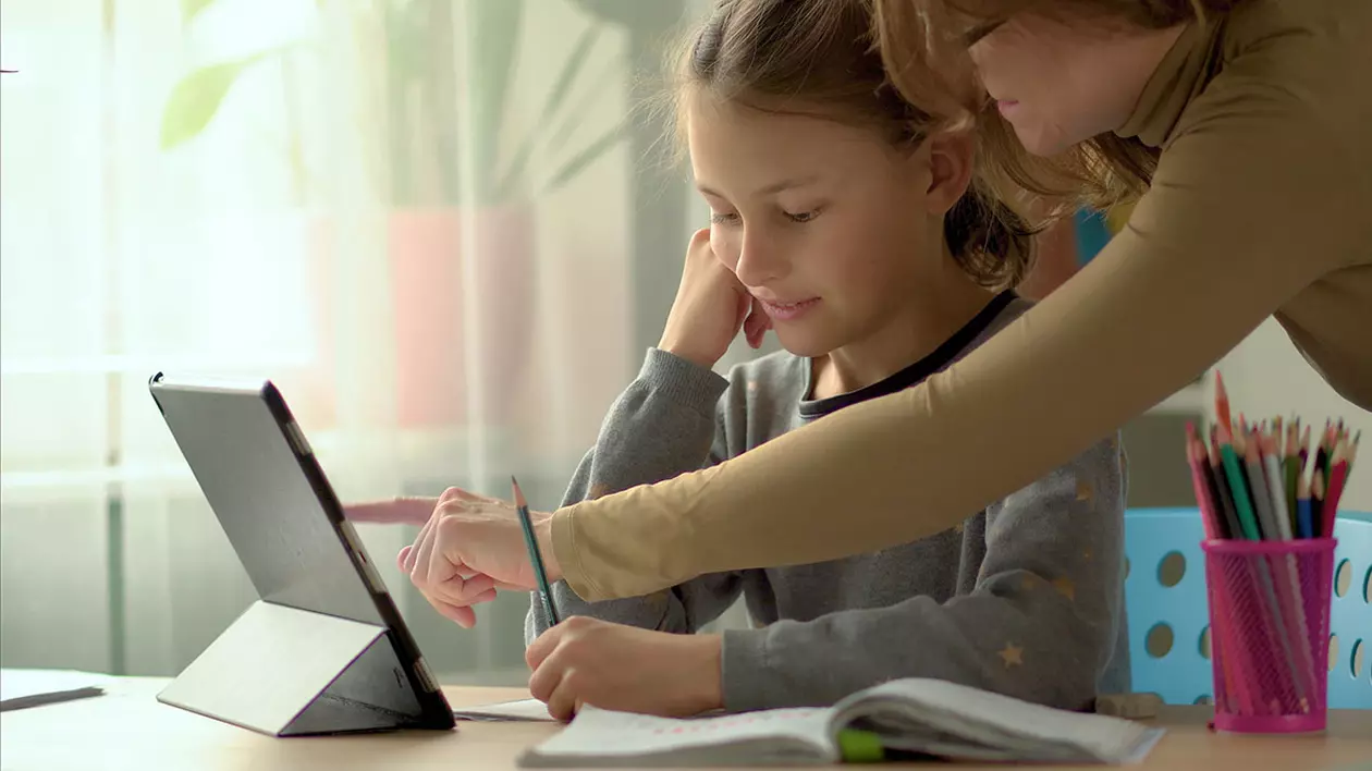 Un fată care învață în sistem homeschooling este ajutată de mama ei la teme