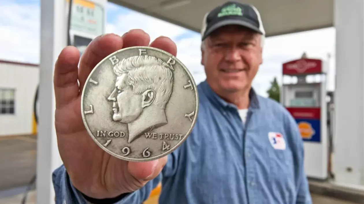 Un bărbat cu șapcă, proprietarul unei benzinării, ține în mână în monedă rară Kennedy Half Dollar, care valorează 3,21 milioane de dolari