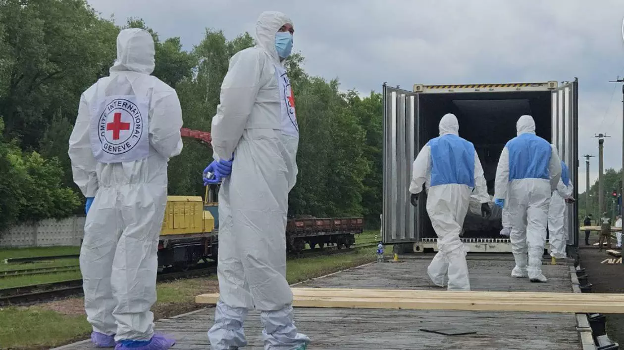 Militari ucraineni îmbrăcați în combinezoane albe așteaptă să ridice cadavrele soldaților morți.