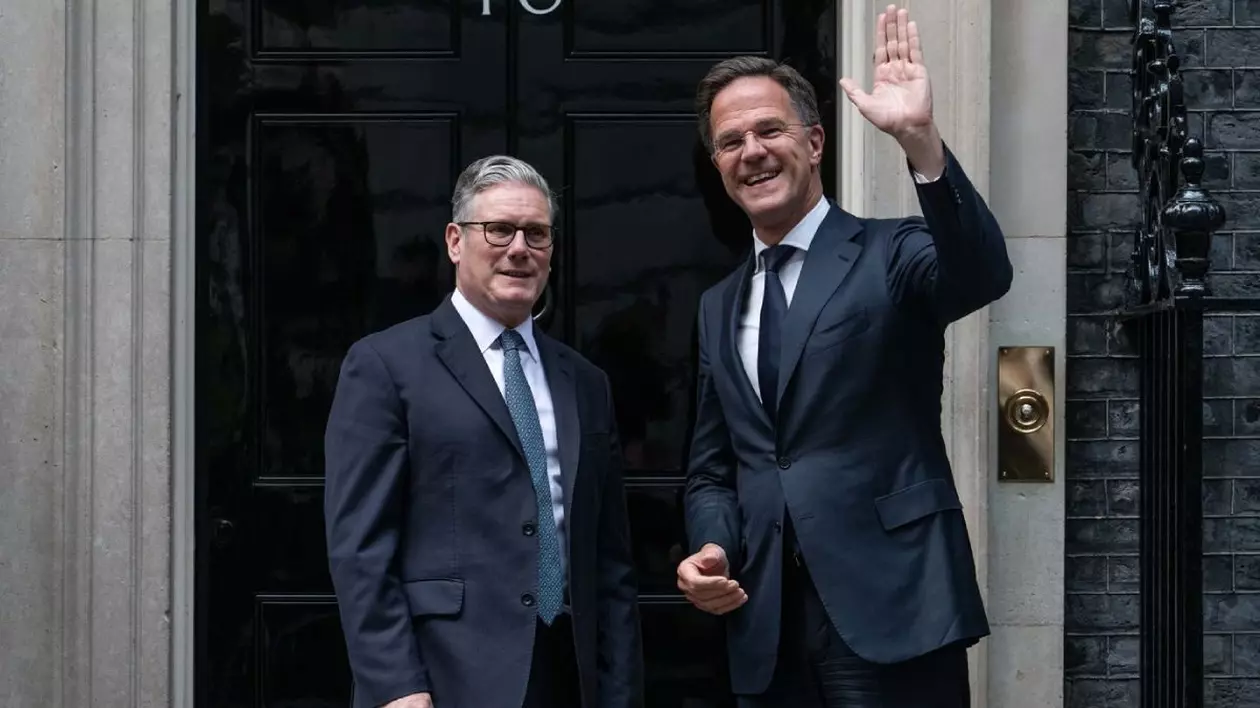 Keir Starmer, stânga, alături de Mark Rutte, cu mana stanga ridicata in semn de salut, dreapta