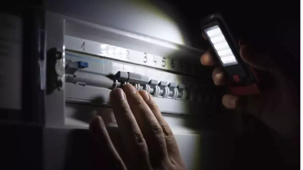 O persoană care verifică un tablou electric cu o lanternă