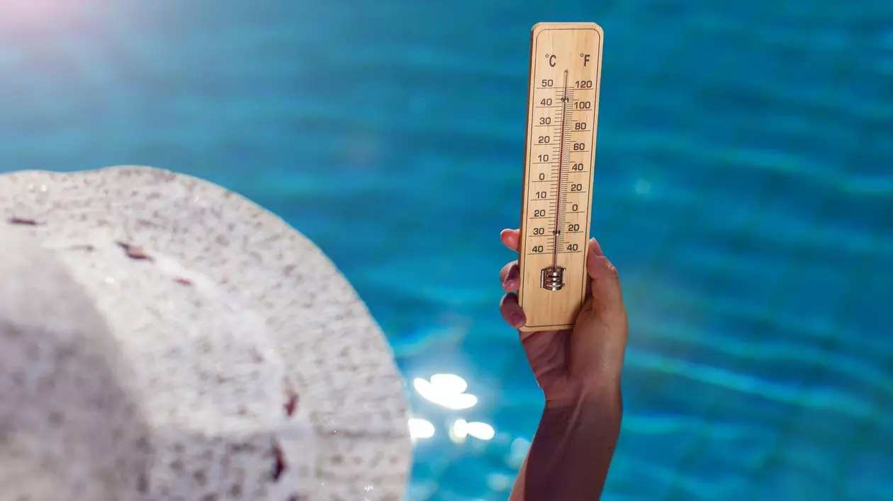 Femeie care ține în mână un termometru, iar în fundal este o piscină.