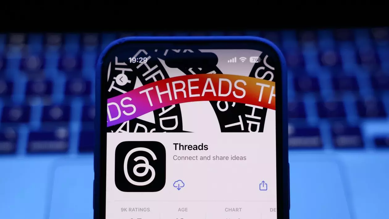 Pagina de pe AppStore a aplicației Threads, deschisă pe un iPhone așezat în fața unei tastaturi de laptop.