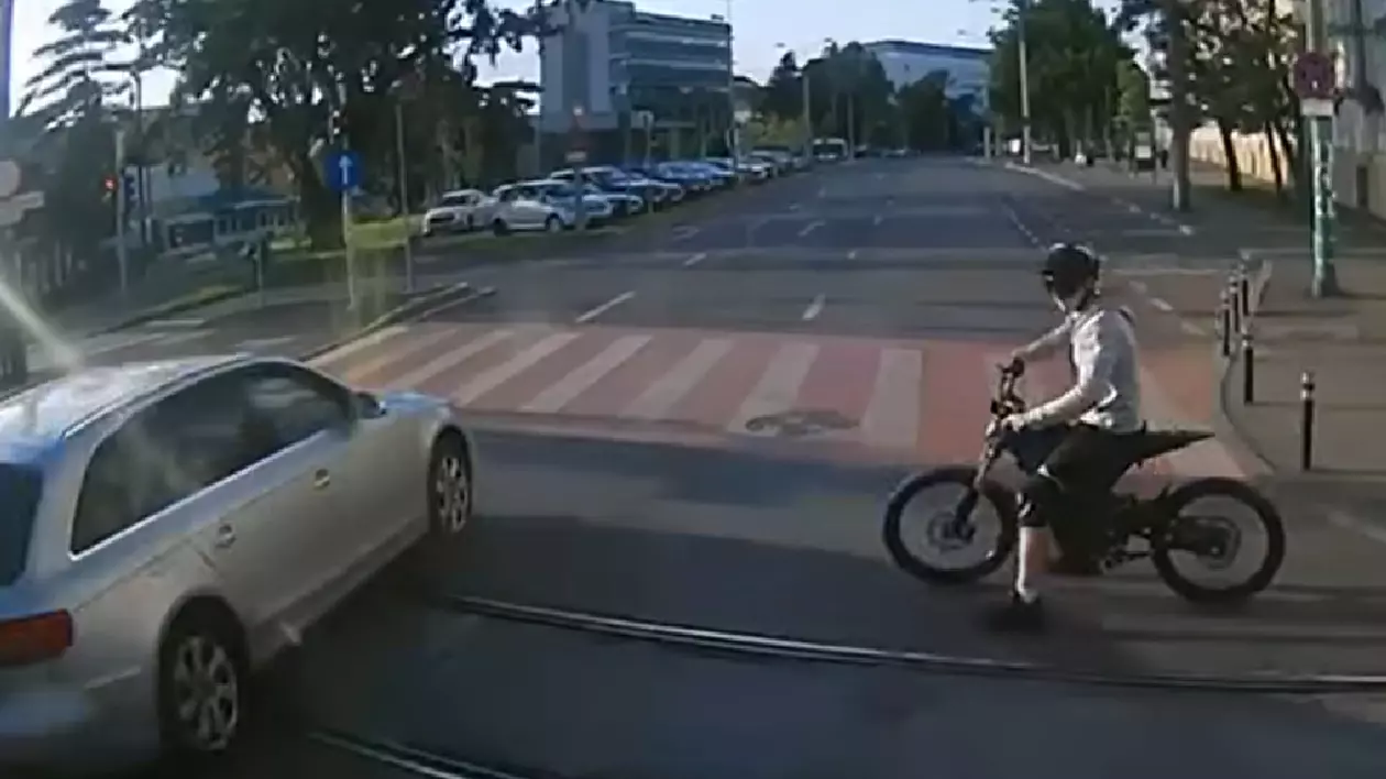 Un copil încearcă să traverseze cu bicicleta pe la o trecere de pietoni și se îndreaptă exact spre o mașină albă care a oprit în ultimul moment