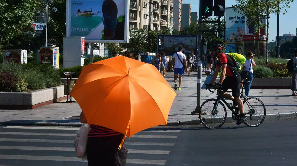 O femeie cu o umbrelă de protecție împotriva caniculei, pe stradă în București, într-o zi caldă de vară.
