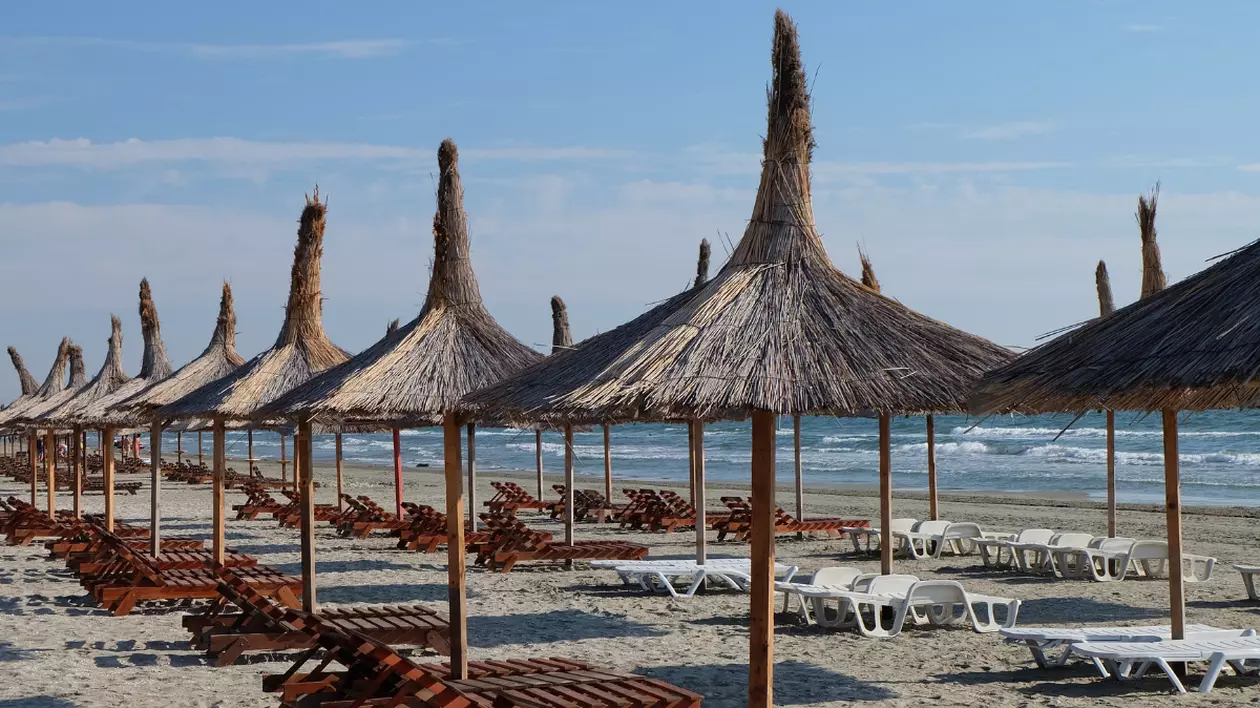 În imagine sunt ilustrate umbrele de paie pe plaja din Mamaia și șezlonguri