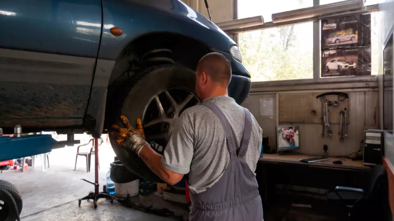 În imagine este ilustrat un mecanic într-un service auto, care verifică roata unei mașini