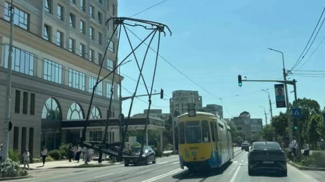 În centrul imaginii se vede un tramvai oprit pe șine, cu pantograful complet desprins și rămas suspendat în aer, agățat de rețeaua de fire de contact.