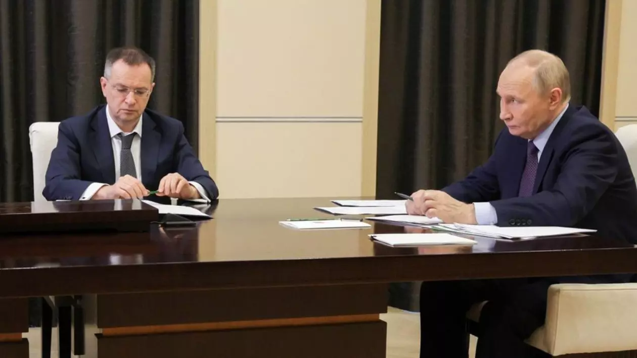 Vladimir Medinsky, stanga, și Vladimir Putin, dreapta, stau la o masa din lemn, cu acte in față