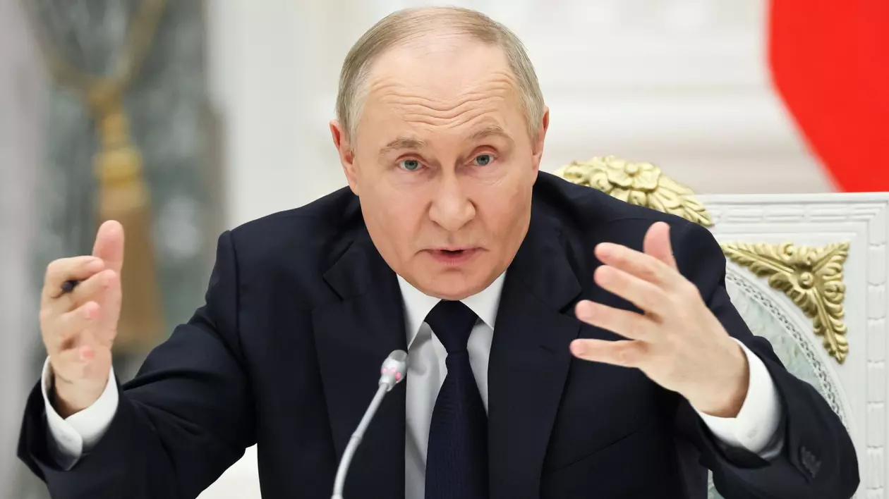 Vladimir Putin surprins vorbind la microfon și având ambele mâini ridicate. Liderul de la Kremlin poartă un sacou negru, o cămașă albă și o cravată neagră