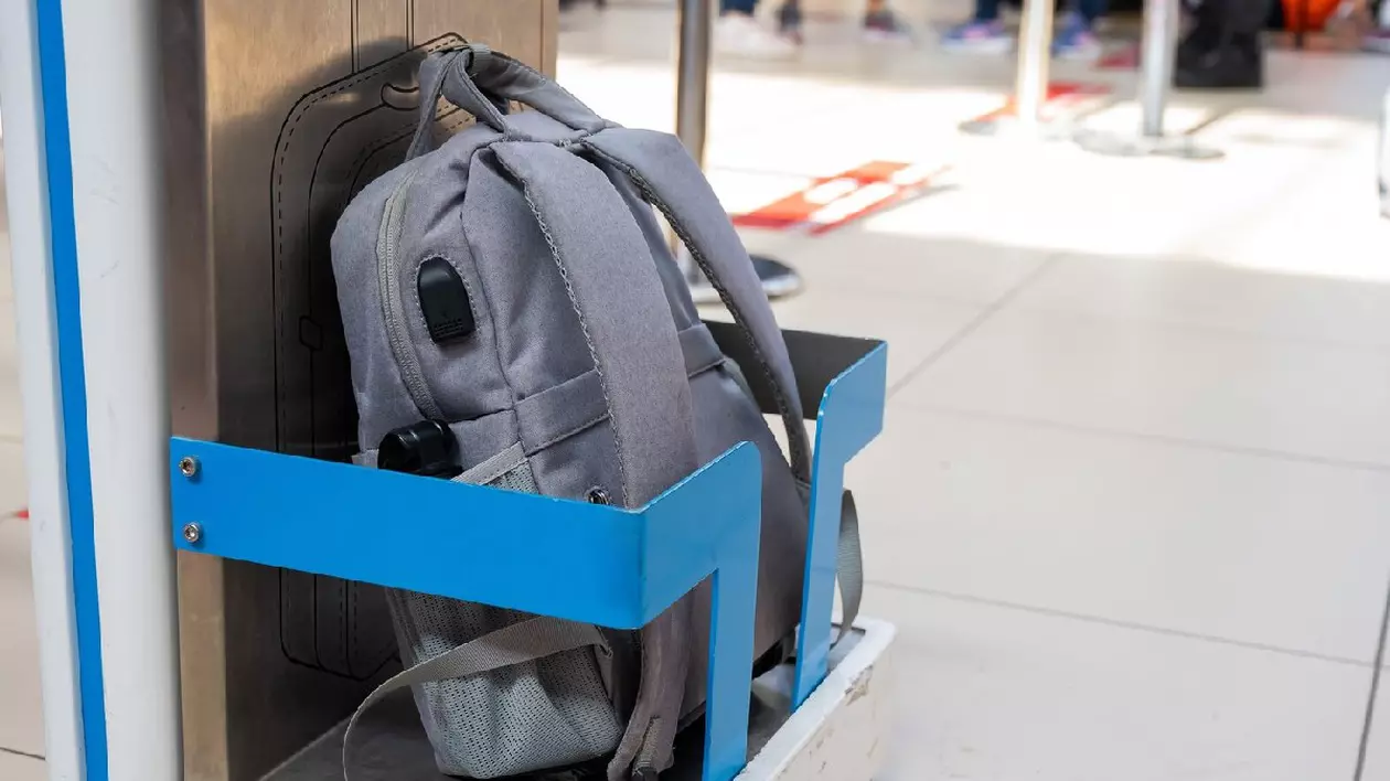 Un ghiozdan gri stă într-un suport metalic albastru pentru verificarea dimensiunii bagajelor de mână la aeroport.