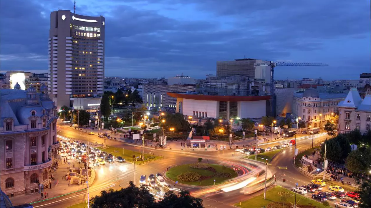 Intersecția de la Universitate în timpul serii, luminile sunt aprinse, iar mașinile circulă cu farurile pornite. Este aglomerație de mașini la semafor