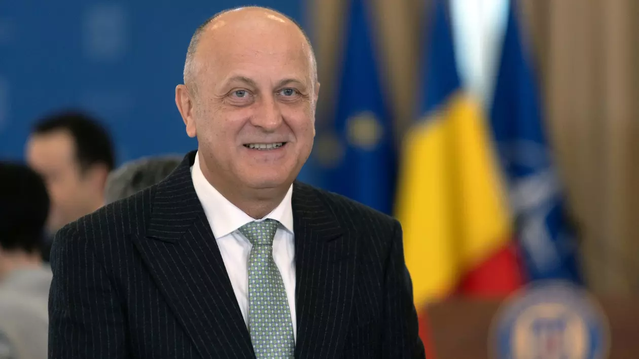 Dan Șucu surprins zâmbind la conferința România OCDE, organizată în aprilie 2025 la Palatul Cotroceni. Poartă un sacou negru, o cămașă albă și o cravată verde cu buline albe