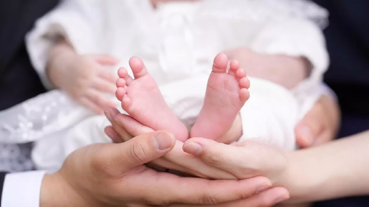 Un prim-plan arată picioarele mici ale unui bebeluș, ținute în mână de părinți