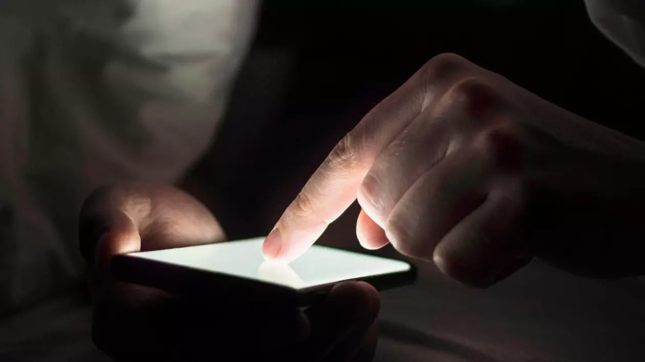 Bărbat care stă pe telefon, ținând degetul arătător lipit de ecranul telefonului mobil care este luminat în alb