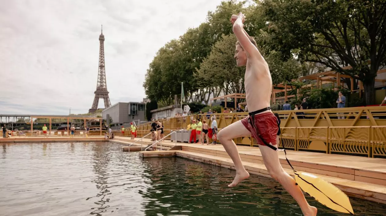 Un tânăr în slip și cu un flotor galben legat de talie sare în fluviul Sena, în timp ce pe fundal se distinge Turnul Eiffel din Paris, 5 iulie 2025