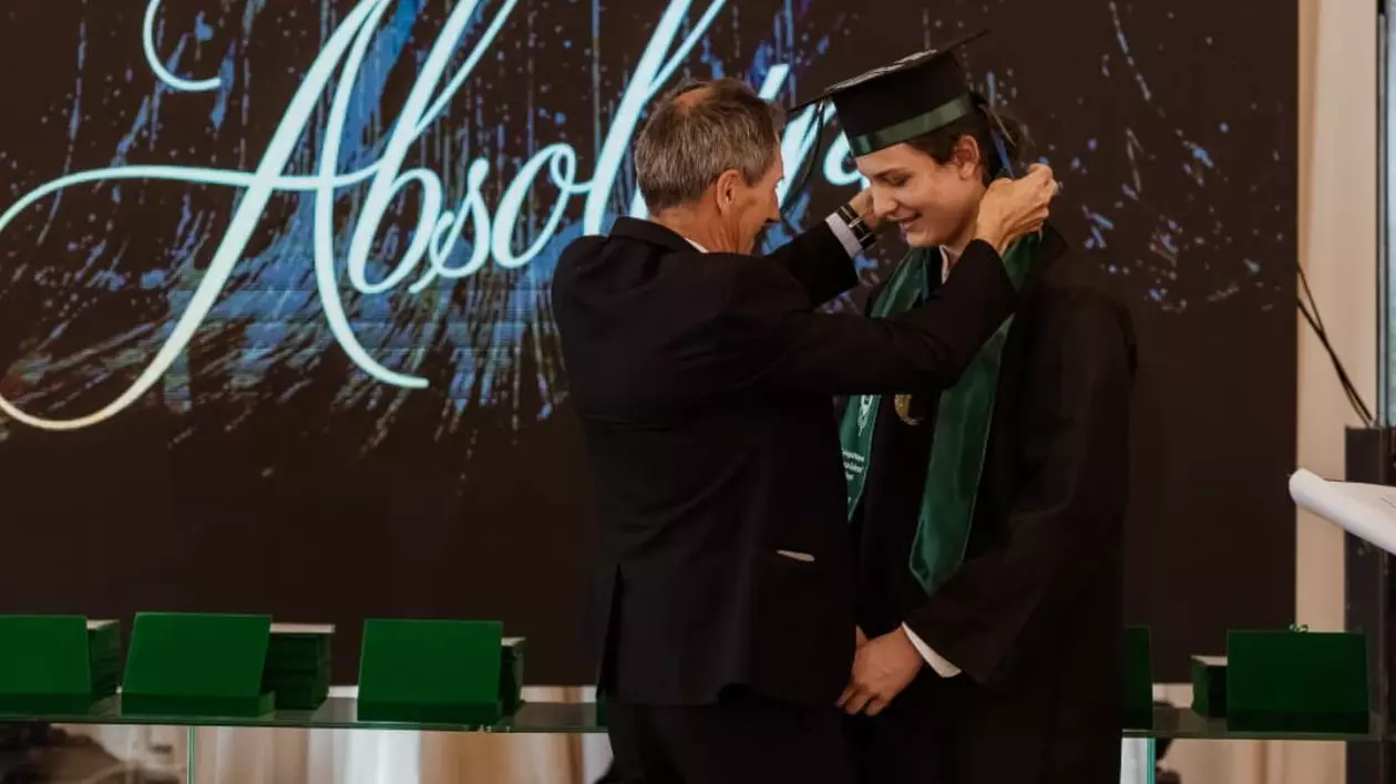 Tudor Vasilescu, elevul de 10, in cadrul ceremoniei de absolvire, inbrîcat in robă negru cu verde, primeste o medalie in gurul gâtului de la un bărbat . Foto Colegiul Național Zinca Golescu Facebook