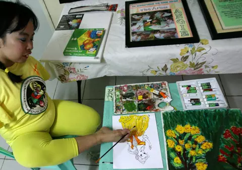 O femeie fără mâini pictează cu picioarele pentru a-şi cumpăra pastile