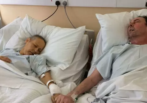 Fotografia care a sfâșiat inimi: Părinți bolnavi de cancer în fază terminală se țin de mână pe patul de spital. Mesajul copiilor lor