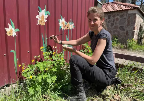 Artă din gloanțe. Un artist plastic desenează flori peste urmele lăsate de cartușe în gardurile din Bucha