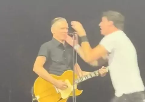 Momentul în care un fan sare pe scenă în timpul concertului lui Bryan Adams, îi smulge microfonul și începe să cânte. Reacția artistului