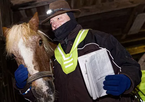 Un bărbat livrează ziarele pe zăpadă și gheață cu ajutorul unui cal care poartă o vestă reflectorizantă, în Germania
