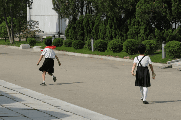 Măsură inedită în orfelinatele din Coreea de Nord. Fetițe din Coreea de Nord, în câmăși albe și cravată roție (de pionier) aleargă pe o alee)