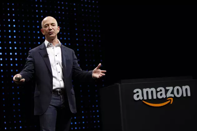 Amazon cumpără Ring, o companie care produce sonerii inteligente și camere de securitate dotate cu asistentul virtual Alexa, cu un miliard de dolari. Jeff Bezos, fondatorul și șeful Amazon, pe o scenă cu logo-ul Amazon pe fundal negru