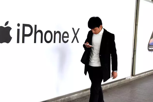 Japonia acuză Apple de comportament anticoncurențial. Un om trece prin fața unui perete pe care scrie iPhone X