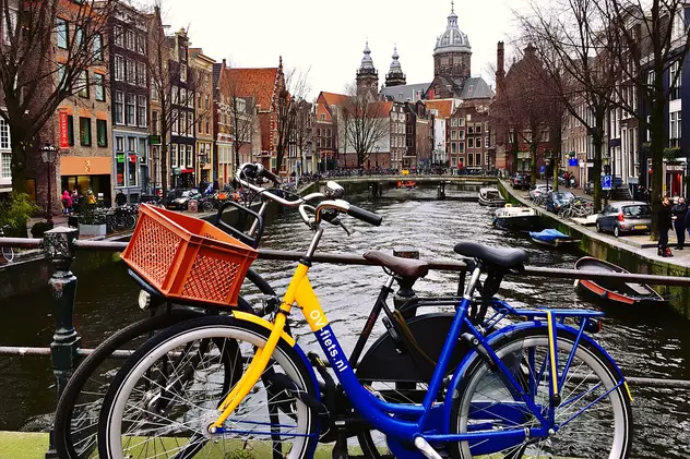 În Olanda nu se mai organizează referendumuri consultative. Fotografie cu orașul Amsterdam, capitala Olandei, cu două biciclete în prim-plan