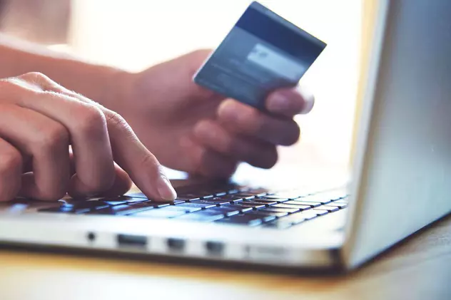 România este pe ultimul loc în UE la achizițiile online. O persoană care face o plată cu cardul bancar, de pe un laptop