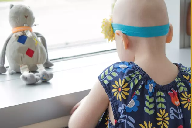 Septembrie este luna conștientizării cancerului în rândul copiilor. Fetiță bolnvă de cancer, cheală și cu o bentiță albastră, se uita pe o fereastră. Pe pervaz este o păpușă