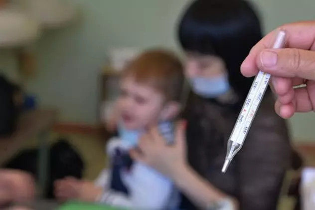 Ar putea să fie declarată epidemie de gripă în România. O mamă își ție copilul bolnav în brațe, în timp ce o asistentă medicală ține un termometru în mână
