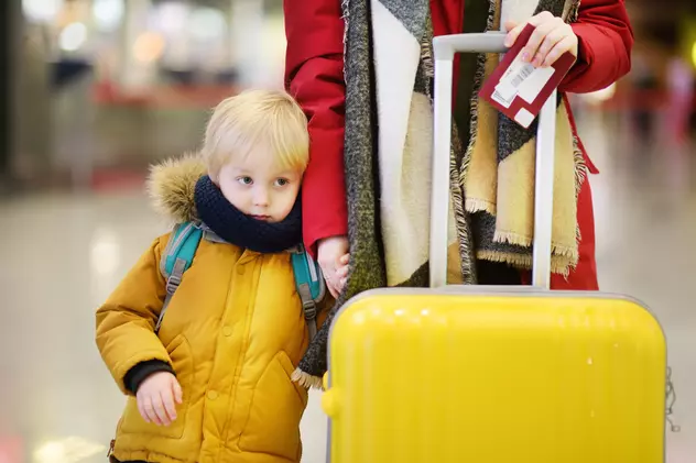 Acte necesare pașaport minor în 2020- Copil în geacă galbenă alături de mamă, care ține pașaportul și trollerul în mână