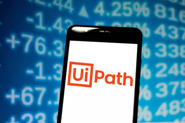 UiPath a strâns 1,34 miliarde de dolari pe bursă. Compania, evaluată la 29 de miliarde de dolari, mai mult decât Carrefour și aproape cât Panasonic. Logo-ul UiPath pe ecranul unui smartphone, cu cifre în spate