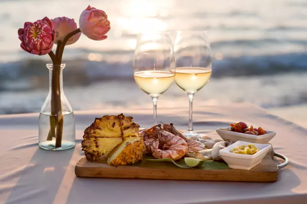 Câte tipuri de vin alb există - Cină romantică la restaurant pe plajă cu vedere la apusul soarelui.