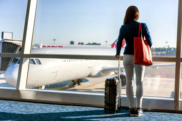 Care sunt cele mai mari companii aeriene din lume în 2022 - O turistă cu bagaje privind apusul de soare pe fereastra unui aeroport.