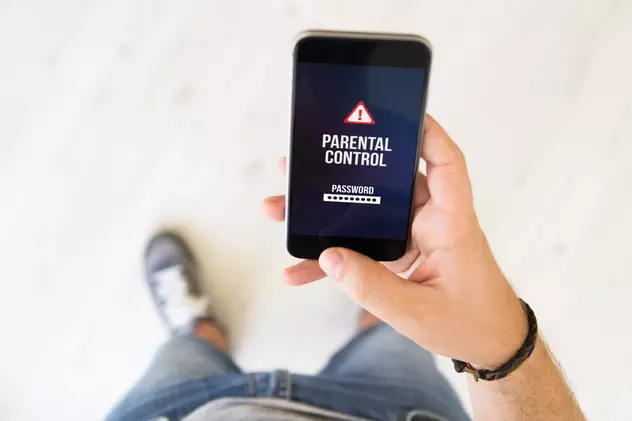 Cum setezi control parental pe telefonul copilului - Un tânăr ţine în mână un telefon mobil cu mesajul control parental afişat pe ecran