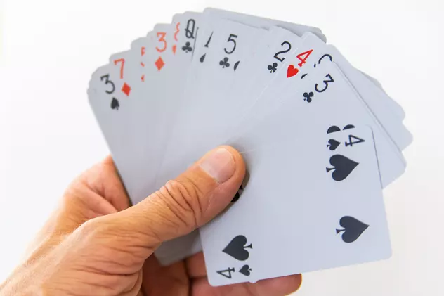 Jocul de canastă – cum se joacă, reguli de bază și modalități de joc - Un bărbat care ţine în mână cărţile de joc la canastă
