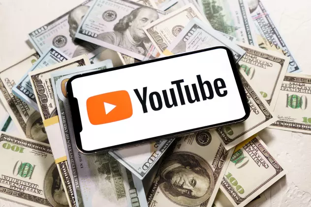Cum poţi să câștigi bani pe YouTube - Imagine cu un telefon ce are pe ecran sigla YouTube şi este aşezat pe un teanc de bani