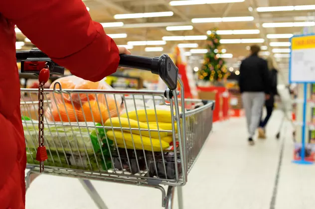 Program magazine de Crăciun 2022 - Imagine cu o femeie cu un cărucior în care îşi pune cumpărăturile de Crăciun, într-un supermarket
