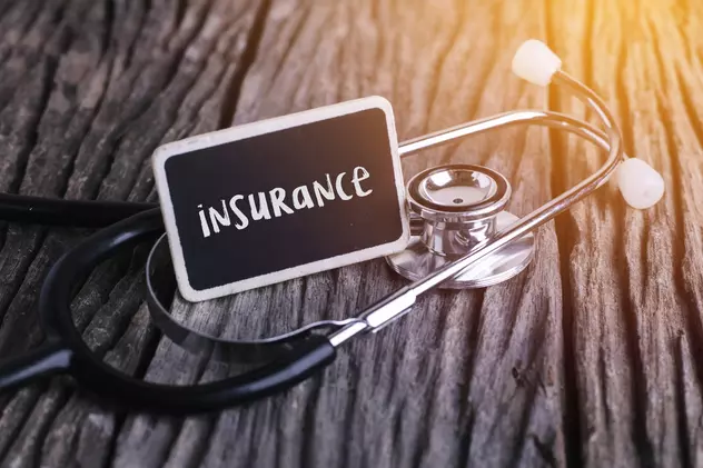 Ce este asigurarea de sănătate privată - Imagine cu un stetoscop pe o masă de lemn, pe care apare si un carton cu mesajul "Insurance", sugerând conceptul de asigurare medicală