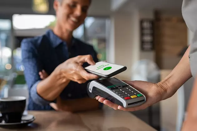 Cum să plăteşti cu telefonul mobil la magazine - Imagine cu o femeie care plăteşte cu telefonul monil la o cafenea
