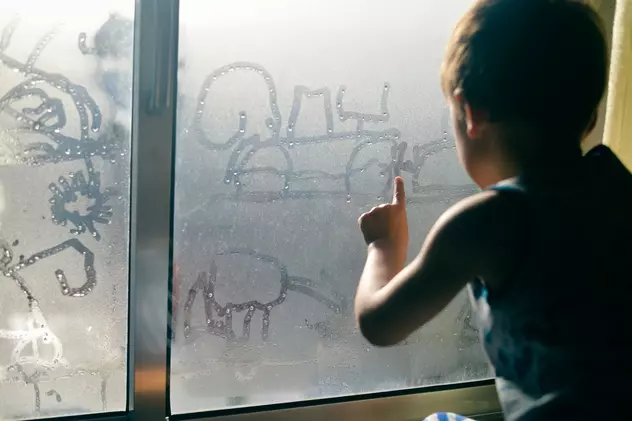 Ce este condensul, de ce apare și cum îl putem evita - Imagine cu un copil care desenează cu mâna pe un geam aburit