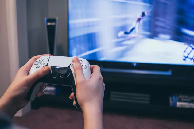 Cât costa PlayStation 5 la eMAG înainte de Black Friday 2023 - Imagine cu un bărbat care ţine în mână controller-ul DualSense al PS5 în faţa televizorului