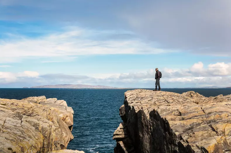 Rosbeg, County Donegal, Ireland weather. 24th April 2016. A walker on Ireland's "Wild Atlantic Way" admires the view over the ocean on a windy but sunny day. In the background is Arranmore Island. © Richard Wayman/Alamy Live News