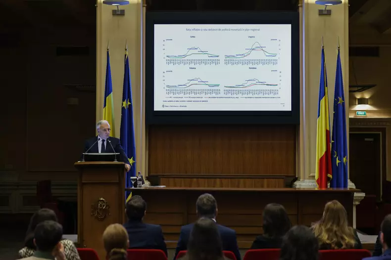 Mugur Isărescu surprins în timp ce vorbește, iar pe fundal sunt afișate grafice cu rrata inflației și rata dobânzii. Foto Vlad Chirea/Libertatea